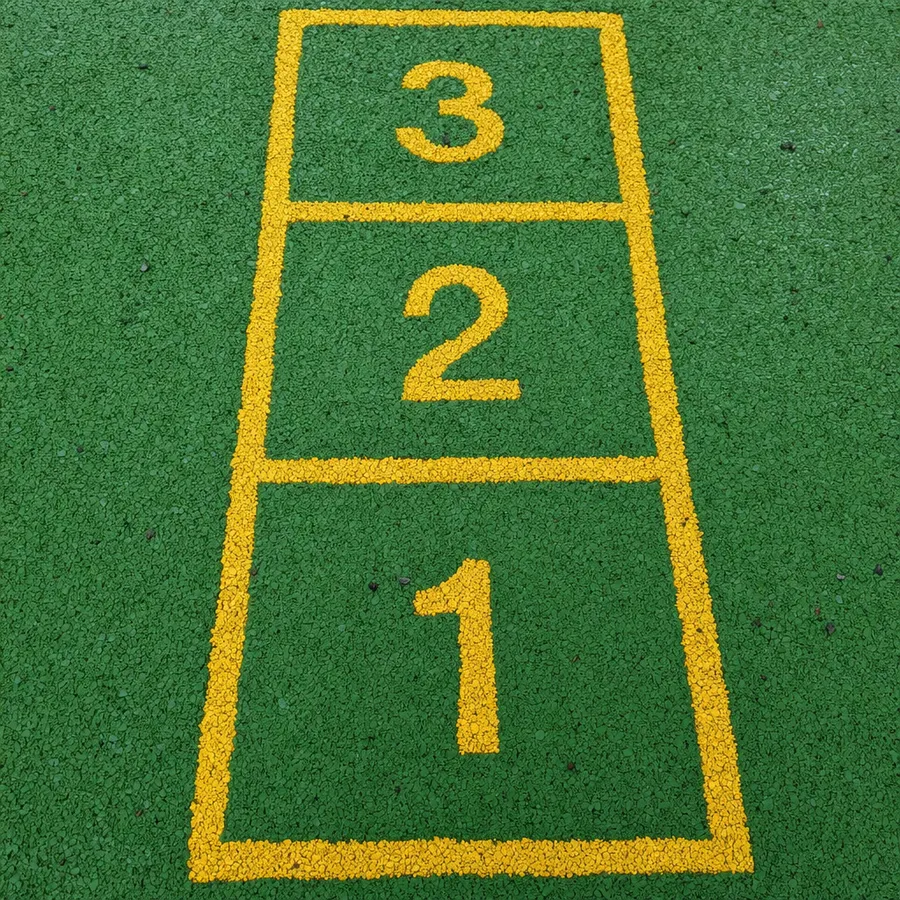 Green wetpour playground surfacing with a yellow hopscotch grid inlaid